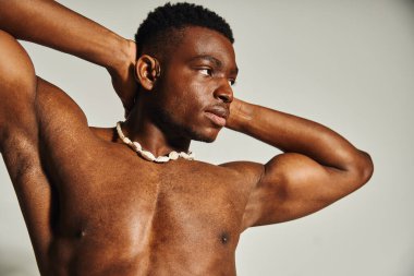 Genç ve yakışıklı bir Afro-Amerikan erkeği kendine güveni tam, tonlu fiziği ve alımlı tavırlarıyla poz veriyor. Arkaplan minimalistik, cesur ifadesini vurguluyor..