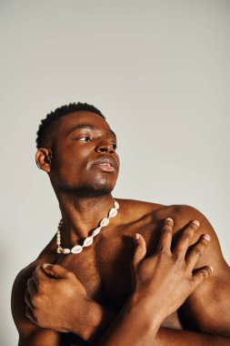 Genç, yakışıklı bir Afro-Amerikan erkeği kendine güveni olan üstsüz poz veriyor. Tarafsız bir zemine karşı duruyor, fiziğini vurgulayarak ve güçlü bir bireysellik duygusu ifade ederek.