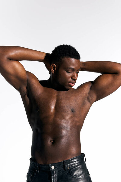 Молодой красивый афроамериканец позирует без верхней одежды, сгибая бицепсы и излучая уверенность. Нейтральный фон подчеркивает его телосложение и простоту момента.