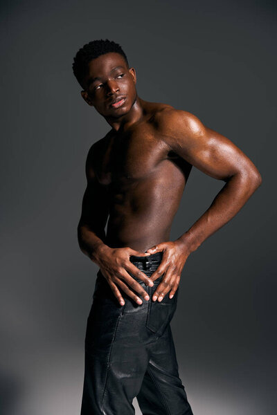 Молодой красивый афроамериканец уверенно стоит, демонстрируя свое тонированное телосложение, игриво положив руку на бедро.