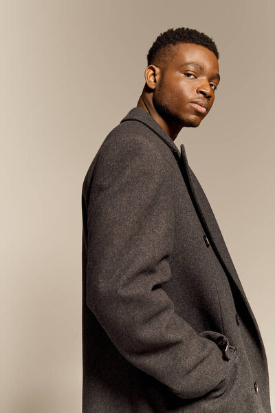 A young handsome African American man poses confidently without a shirt, showcasing his physique. The neutral backdrop enhances his stylish demeanor and strong presence during the indoor shoot.