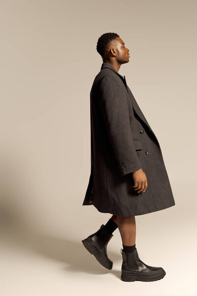 Молодой красивый афроамериканец стоит высокий и уверенный в себе, позируя без верхней одежды в стилизованной обстановке.