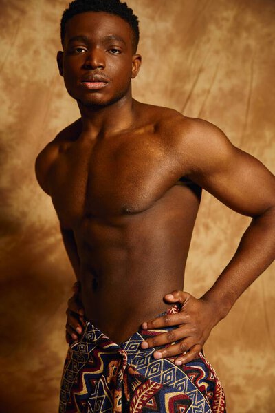 In a captivating artistic backdrop, a young handsome African American man poses confidently. With a bare chest and a stylish wrap, he exudes charisma and strength, embodying vibrant energy.