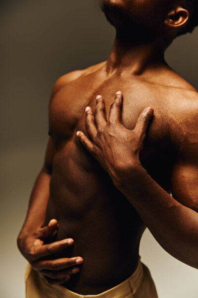 Молодой красивый афроамериканец уверенно позирует без рубашки, подчеркивая его тонированное телосложение. Сцена запечатлевает момент самовыражения и артистизма в студии.
