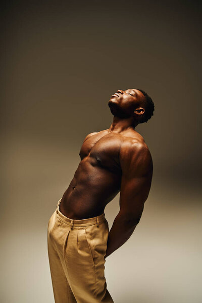 Молодой привлекательный афроамериканец уверенно стоит со сводчатой спиной. Его сильное телосложение выделяется на мягком фоне.