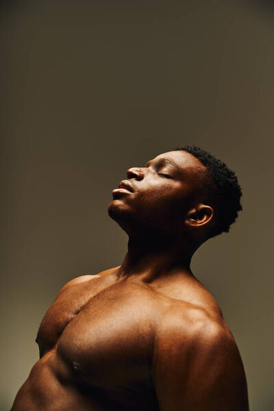 Молодой и красивый афроамериканец позирует без верхней одежды в минималистском окружении.