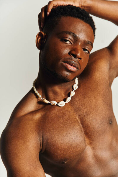 A young, handsome African American man poses topless with a stylish necklace around his neck.