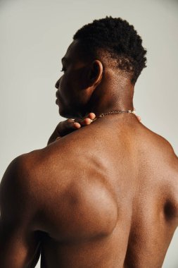 Yakışıklı bir Afro-Amerikan erkeği, fiziğine dikkat çekerek gömleksiz poz veriyor. İfadesi güç ve kararlılık yayıyor, ilham verici bir atmosfer yaratıyor..