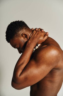 Üstsüz poz veren, fiziksel ve sanatsal ifadesini sergileyen Afro-Amerikan bir adamın büyüleyici anı. İçerideki dingin ortam, bu çarpıcı portrenin görsel etkisini arttırır..