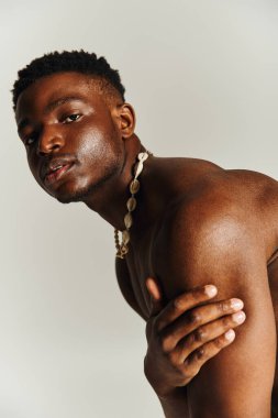 Genç, yakışıklı, Afro-Amerikan bir adam gömleksiz poz veriyor. Güçlü özellikleri ve eşsiz bir kolyesi var. Yumuşak arka plan çarpıcı varlığını ve kişiliğini arttırır..