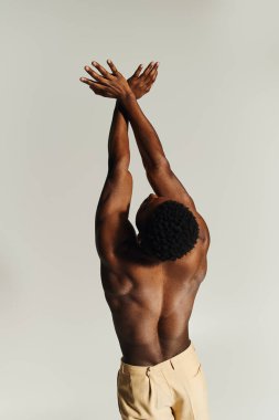 Genç ve yakışıklı bir Afro-Amerikan erkeği kollarını başının üstünde birleştirerek üstsüz poz veriyor..
