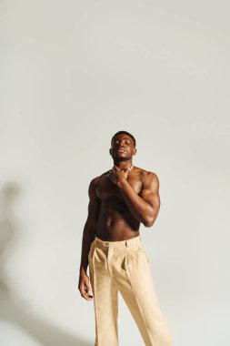 Yakışıklı, Afro-Amerikan bir adam kendine güvenerek şık ve minimalist bir ortamda üstsüz poz veriyor..