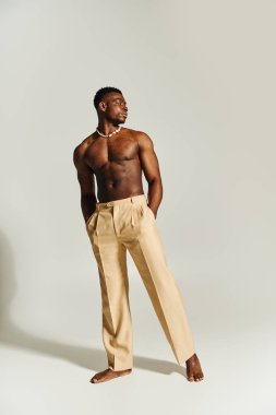 Genç, çarpıcı bir Afrikalı Amerikalı kendine güvenen bir duruş sergiliyor, kaslı fiziğini sergiliyor. Açık renkli pantolonun içinde yalınayak dururken, minimalist bir arkaplana karizma yayıyor..