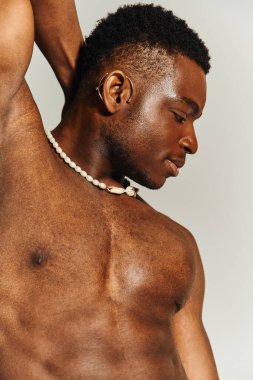 Genç bir Afrikalı Amerikalı kendine güvenen bir pozla fiziğini sergiliyor. Üstsüz duruyor, şık bir kolye takıyor. Arkaplan basit, çarpıcı özelliklerini ve karizmasını vurguluyor..