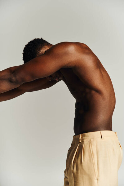 Молодой красивый афроамериканец демонстрирует свою физическую форму, позируя без верхней одежды в простой студийной обстановке, воплощая силу и уверенность во время творческого флешмоба..