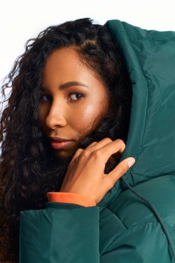 A stunning woman with curly hair gazes confidently, wearing a chic green jacket with a hood. clipart