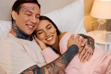 Yumuşak bir yatakta sarılan mutlu bir çift, kendi mekanlarında sıcaklığı ve sevgiyi paylaşıyor..