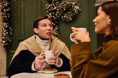 Büyüleyici bir çift sıcak içeceklerle samimi anlar paylaşırken etrafı şenlikli bir dekorla çevrili.