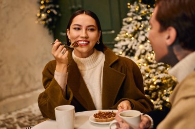 A young couple shares sweet desserts in a cozy cafe filled with festive decor. clipart