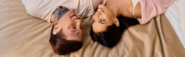 A loving couple lies closely together, laughing and sharing tender moments on a soft bed.
