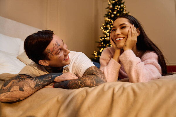 Couple lies on bed, sharing joyful moments and smiles in warm holiday atmosphere filled with love.