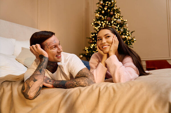 A couple shares smiles while cozying up by their lovely Christmas tree.