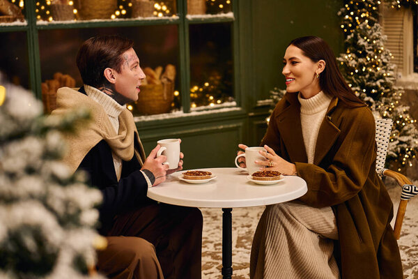 Young couple enjoys hot drinks together, surrounded by festive decorations on a snowy evening.
