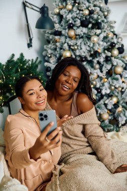 İki kadın süslü bir Noel ağacının yanında selfie çekerken keyifli bir anın tadını çıkarıyorlar.