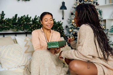 A special moment of joy as two women share a gift amidst festive decorations in a cozy space. clipart