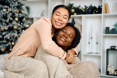 Two women share a tender moment, wrapped in a blanket, surrounded by festive decorations. clipart