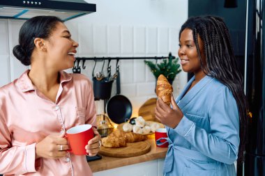 İki kadın kahvaltıdan zevk alır, güler ve sıcak bir mutfak ortamında hamur işlerini paylaşırlar..