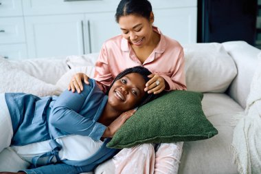 Two women enjoy each others company while lounging comfortably in their stylish living room. clipart