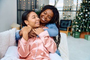 A lesbian couple embraces joyfully in a festive, beautifully decorated area with lights. clipart