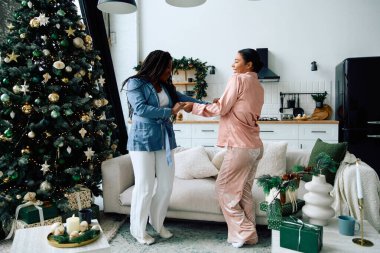 İki kadın, Noel ağacının yanında, şenlikli bir şekilde dans edip, aşkı ve neşeyi kutluyorlar..