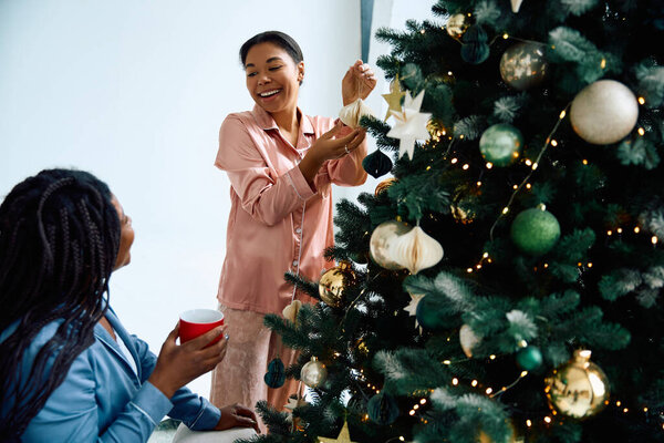 Two women share laughter while decorating a Christmas tree, creating a warm festive atmosphere.