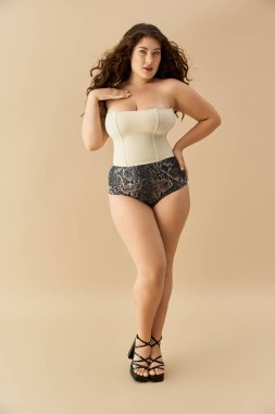 Genç ve cüsseli bir kadın yumuşak bir arka planda kendine güvenen iç çamaşırlarıyla poz verir..