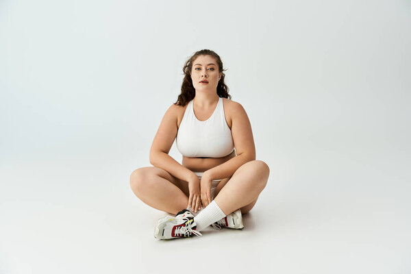 A young plus size woman poses confidently, showcasing trendy underwear in a minimalistic setting.
