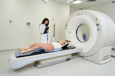 Parlak bir hastane odasında, bir doktor hastanın MRI taramasına hazırlanmasına yardımcı olur..