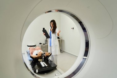 Bir kadın doktor, radyoloji bölümünde MRI taraması sırasında hastasına talimat verir..