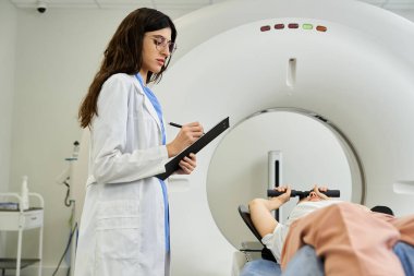 Laboratuvar önlüklü bir doktor, hastane odasında MR çektiren bir hastayı izliyor..
