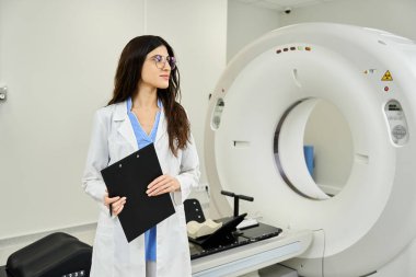 An attractive doctor stands confidently near an MRI machine, preparing for medical diagnostics. clipart