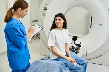 Laboratuvar önlüklü bir kadın, bir sağlık merkezinde bir hastayla MRI prosedürünü tartışıyor..