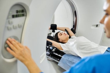 Hasta teşhis için MRI makinesinde yatarken kadın doktor ayarları kontrol eder..