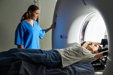 Laboratuvar önlüklü bir kadın doktor hastaya hastanede MRI makinesinin içinde rehberlik ediyor..