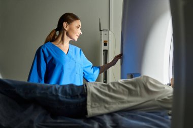 Laboratuvar önlüklü yetenekli bir doktor güvenlik ve rahatlık için MRI makinesindeki bir hastayı kontrol ediyor..