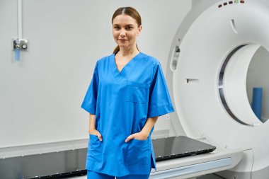 Mavi önlüklü kendine güvenen kadın doktor MRI makinesinin yanında duruyor..