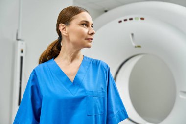 Mavi önlüklü kendine güvenen kadın doktor MRI makinesinin yanında duruyor ve işine odaklanıyor..