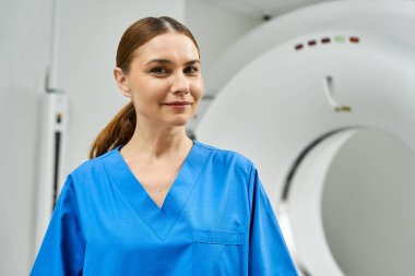 Mavi önlüklü kadın doktor hastane ortamında MRI makinesinin yanında duruyor..