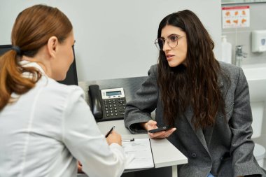 Bir jinekolog, klinik ortamdaki bir kadın hastayla sağlık konularını tartışıyor..
