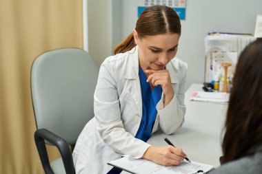 Laboratuvar önlüklü bir jinekolog çağdaş bir klinikte hastasına dikkatle danışıyor..